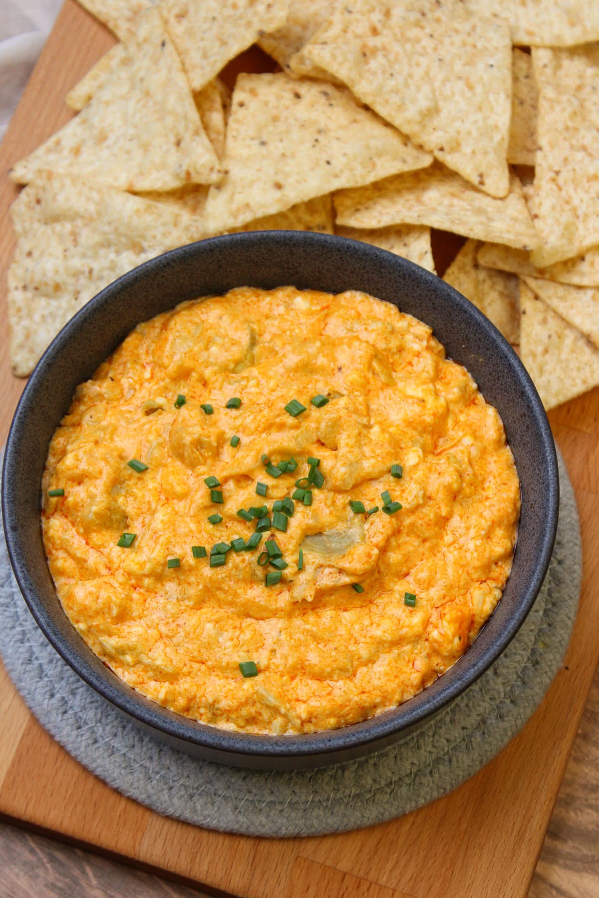 A stoneware bowl of hot buffalo artichoke dip served with tortilla chips.