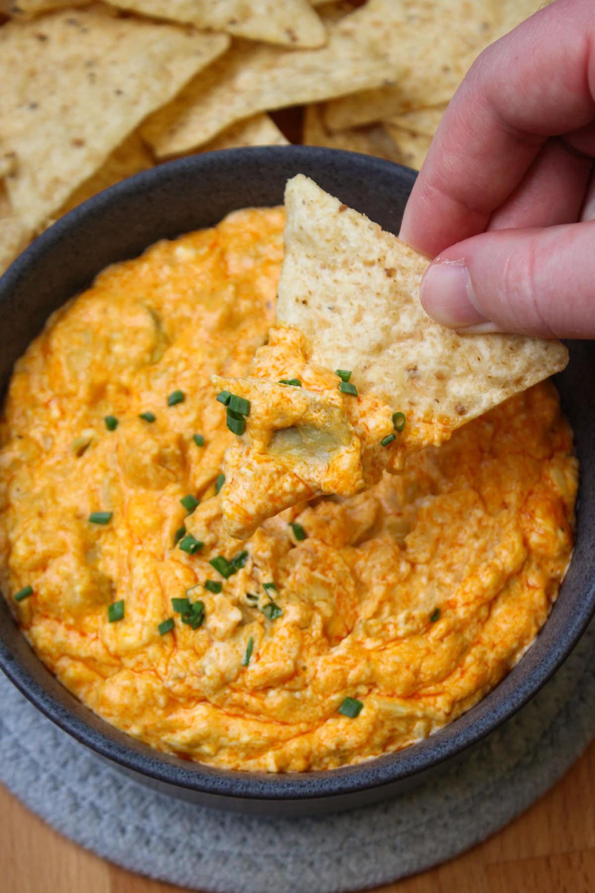 A tortilla chip dipped in cheesy buffalo artichoke dip garnished with chives.