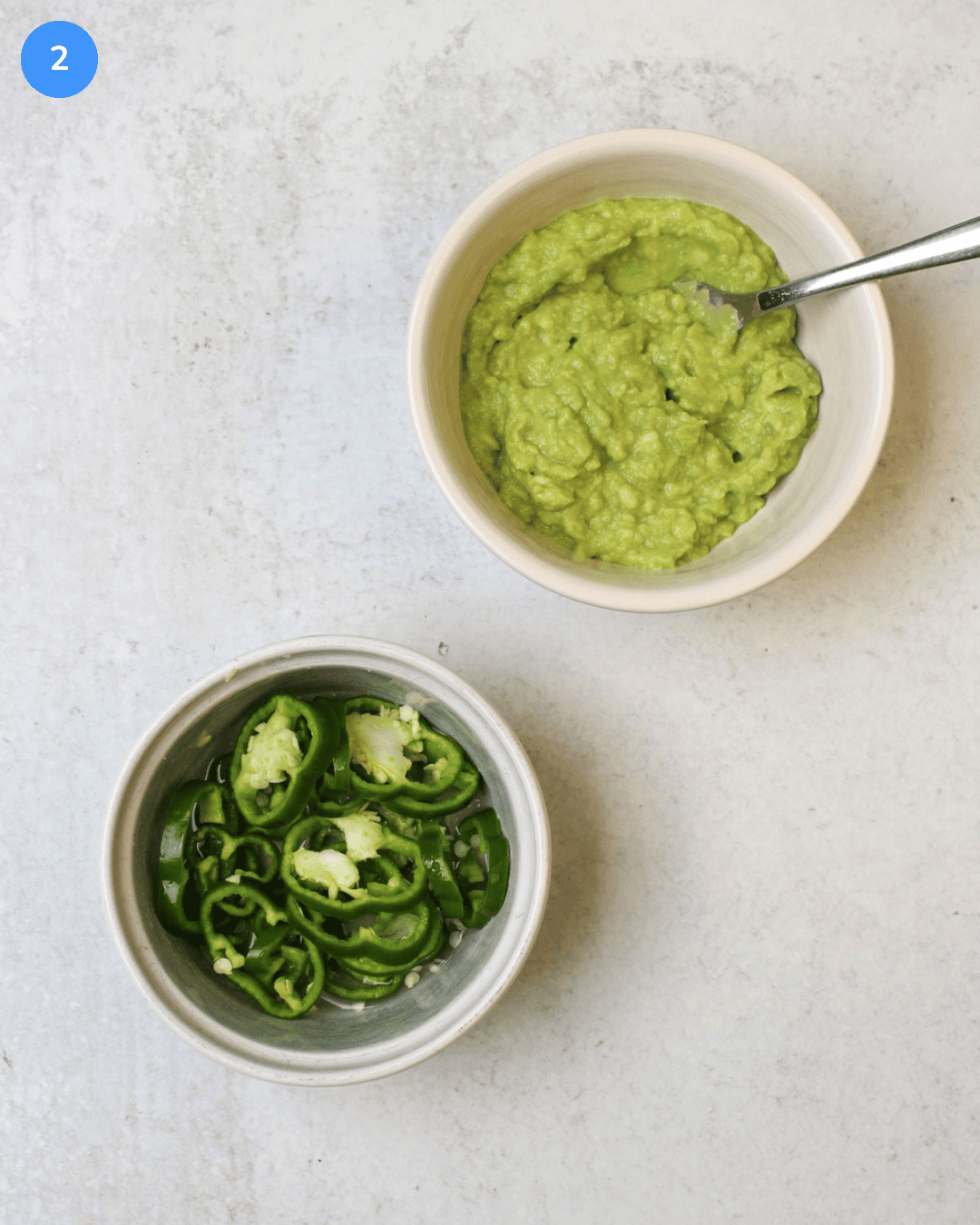 A bowl of mashed avocado and a bowl of anaheim pepper wheels quick pickling in lime juice and salt.