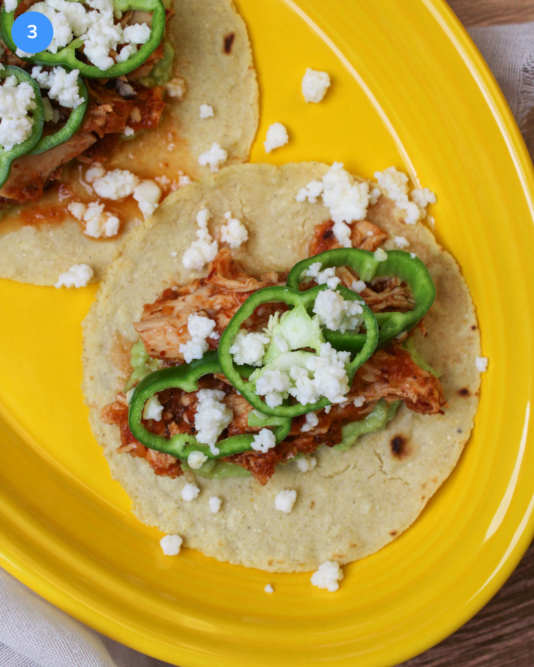 A freshly assembled chicken tinga taco on a corn tortilla with quick pickled anaheim pepper wheels and queso fresco.