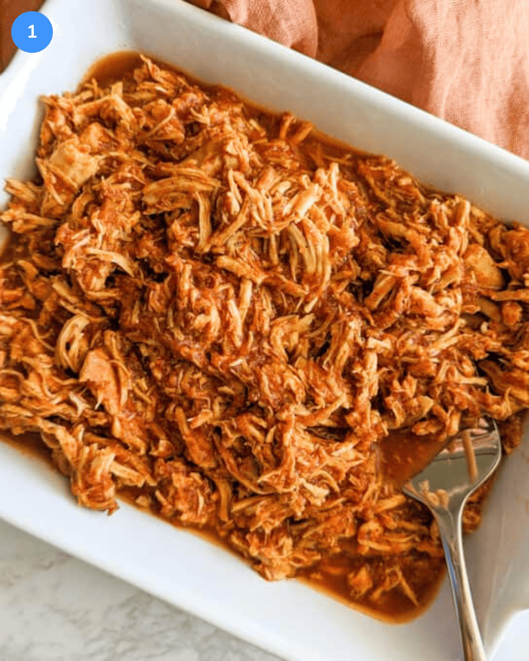 A white ceramic baking dish filled with shredded chicken tinga.
