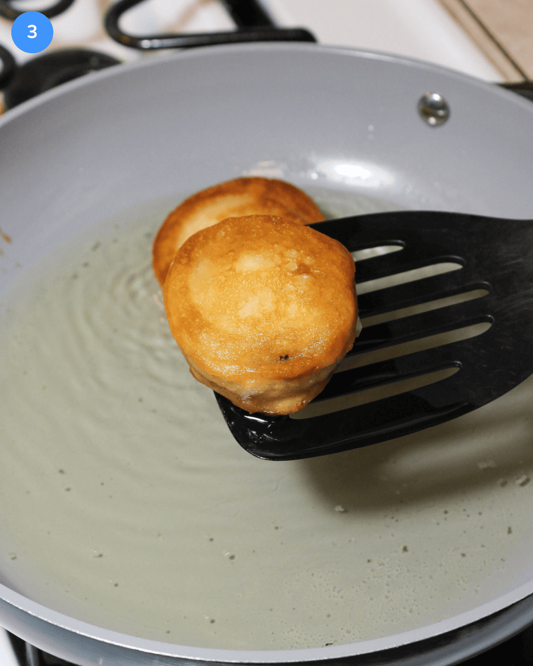 A golden brown fried oreo being removed from hot oil in a pan with a slotted spatula.