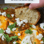 Crusty white bread being dipped into a freshly made skillet of green shakshuka with goat cheese and cilantro, with a title overlaid.