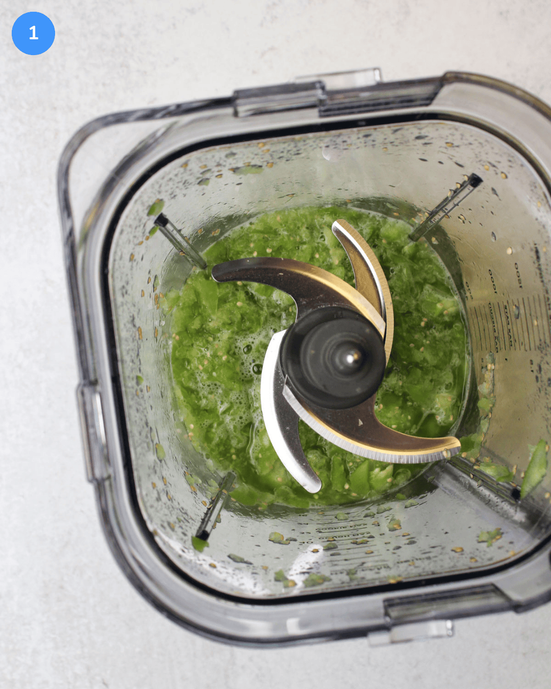 Tomatillos lightly blended in a large blender, juicy with some chunks.