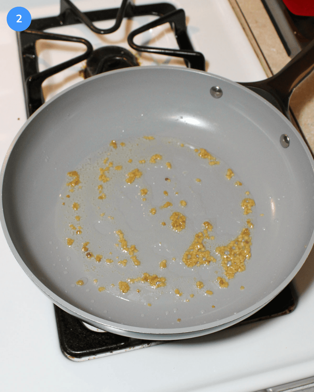 Minced garlic cooking in oil in a ceramic frying pan on the stove.