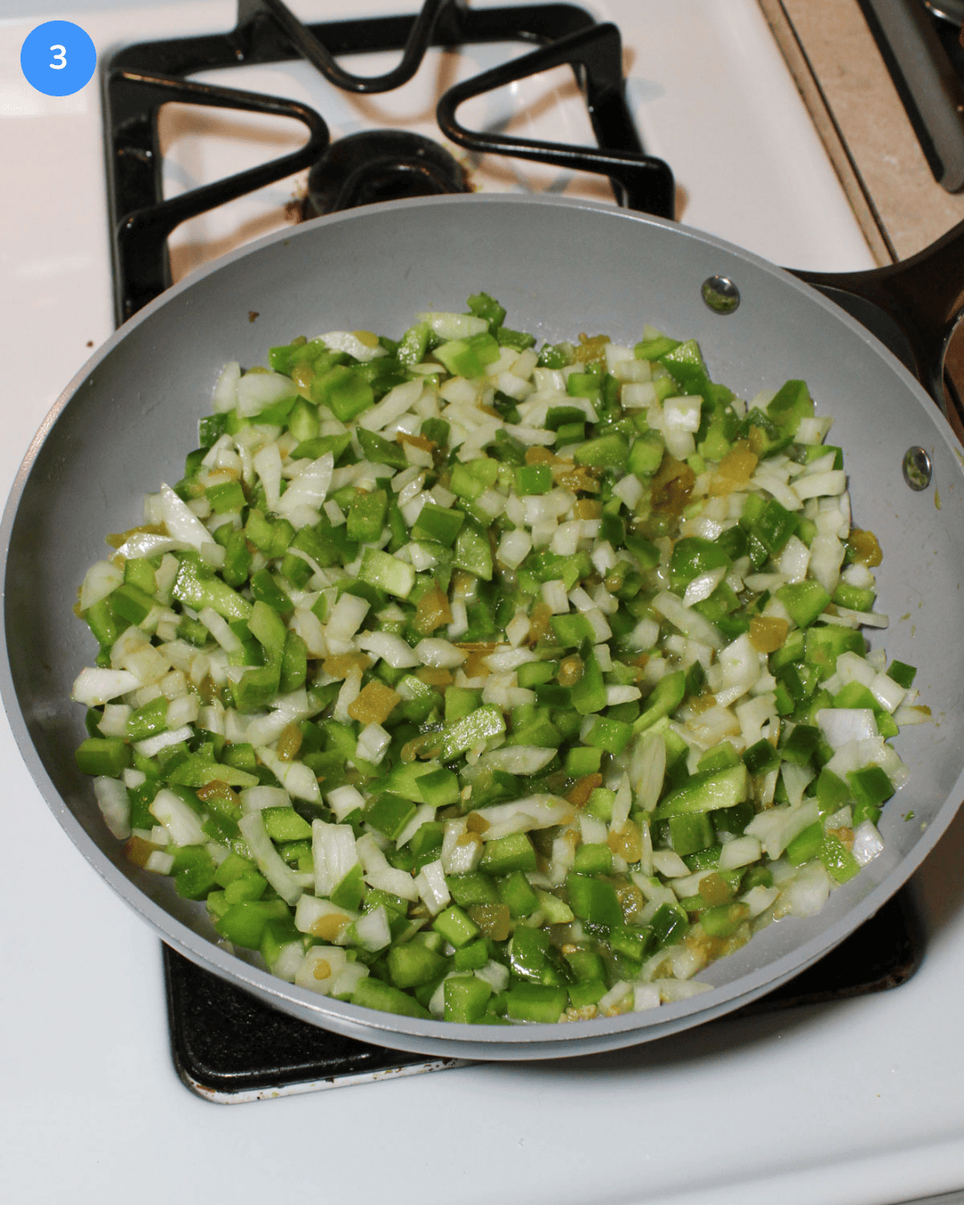 Diced green peppers, green chilies, and white onion cooking in a ceramic frying pan on the stove.