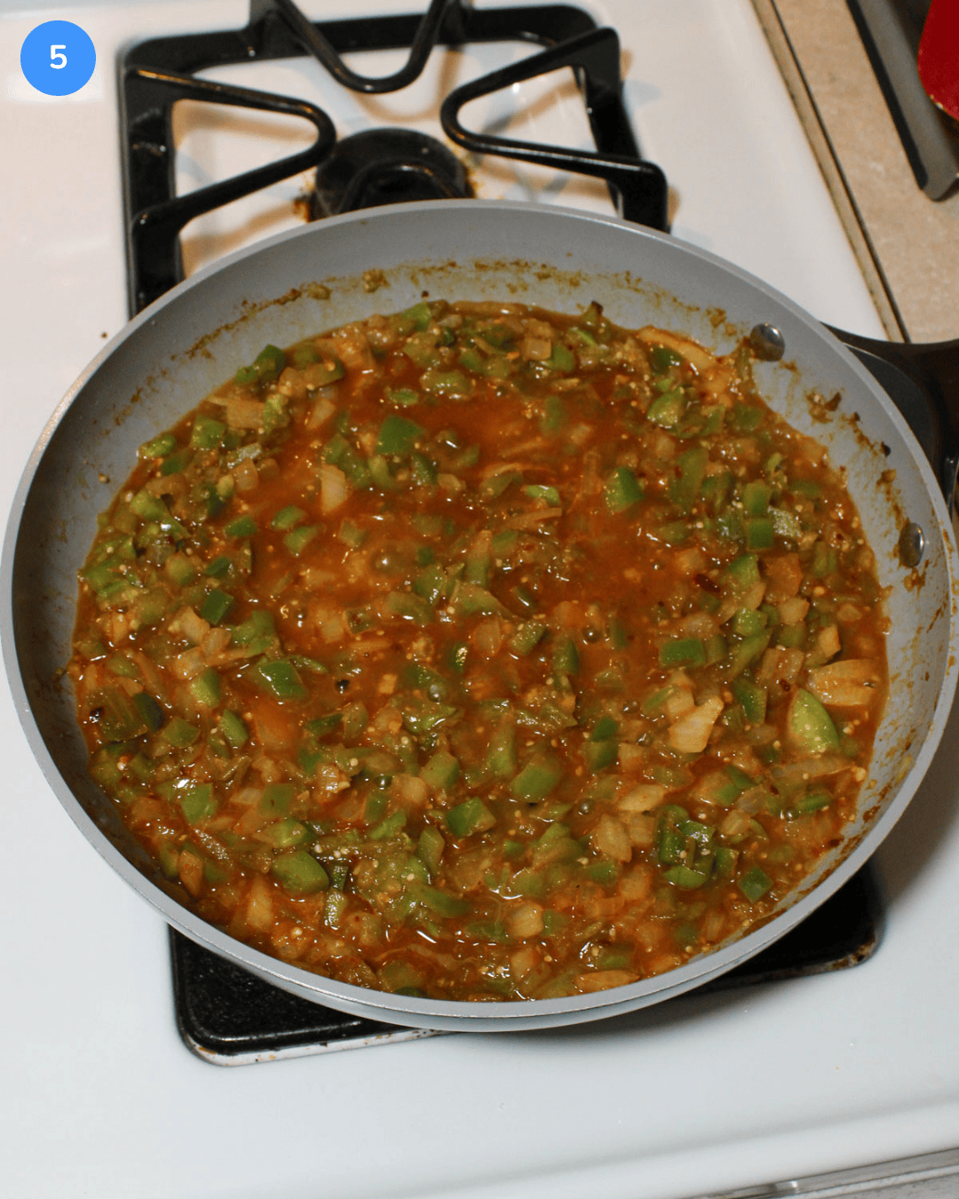 A tomatillo and green veggie stew simmering in a ceramic frying pan on the stove.