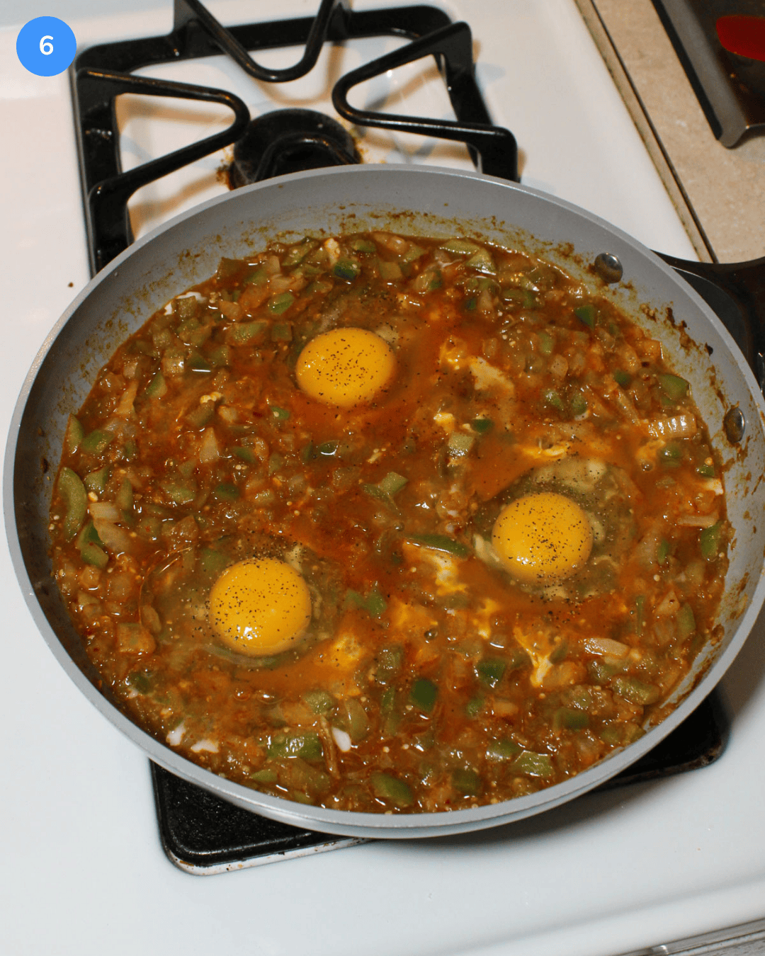 A tomatillo and veggie stew with raw eggs cracked into it simmering on the stove.