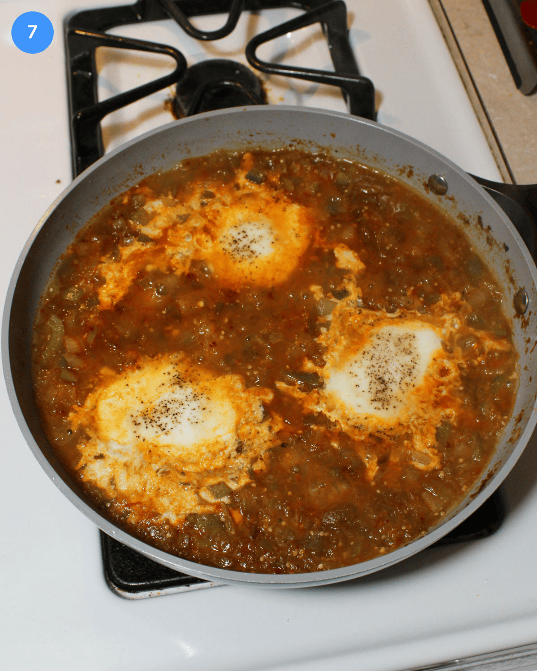 A tomatillo and egg stew cooking in a ceramic frying pan on the stove.