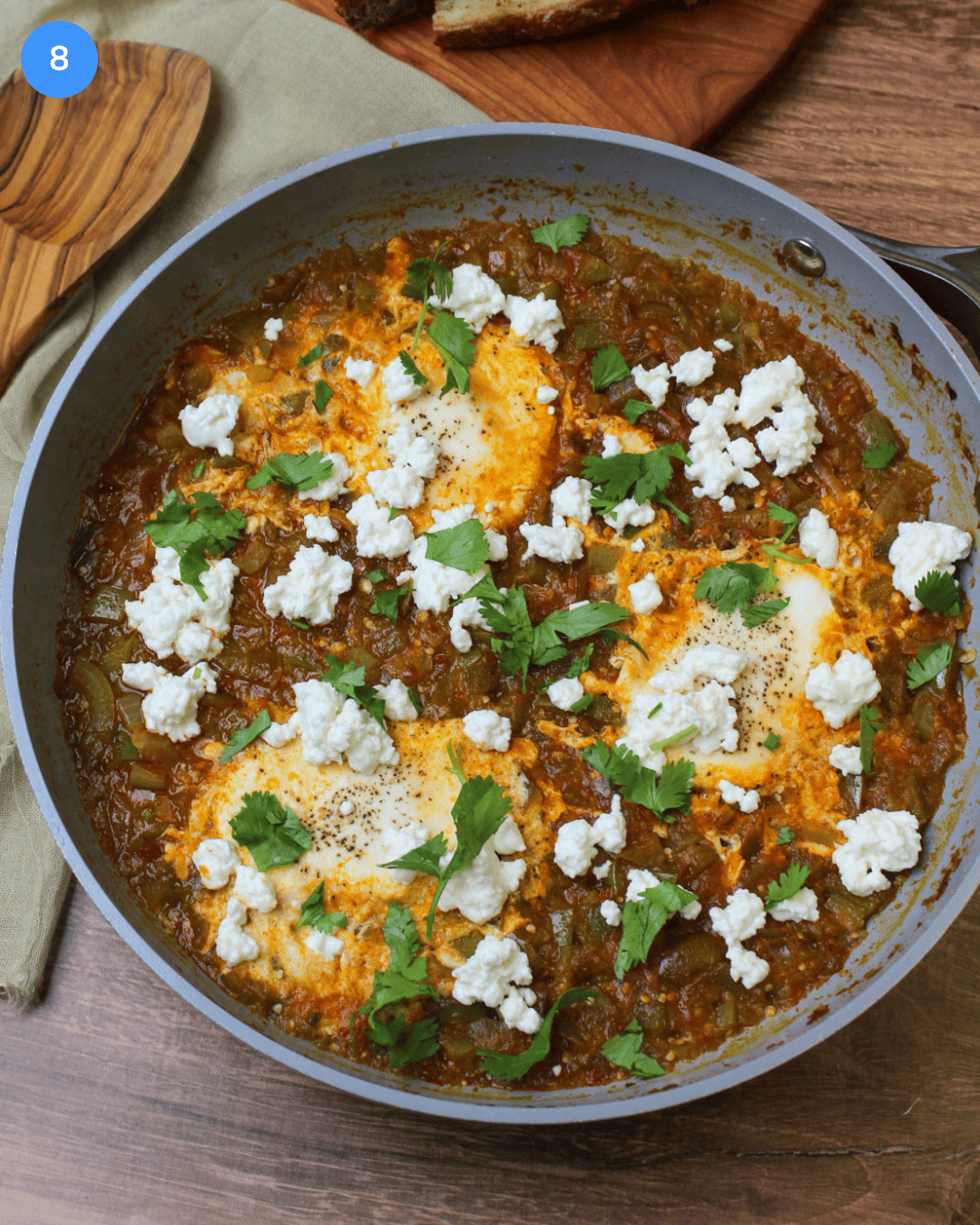 A ceramic skillet of green shakshuka garnished with cilantro and goat cheese crumbles.