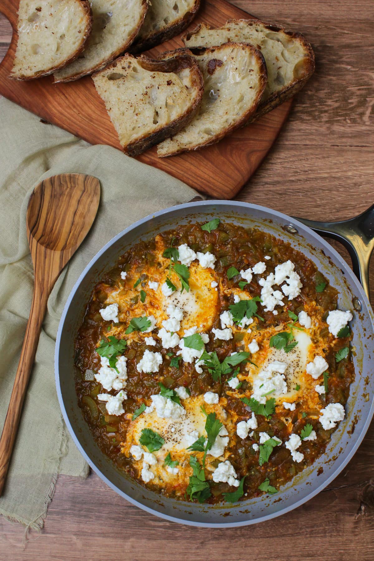 A ceramic skillet of freshly made green shakshuka served alongside crusty white bread.