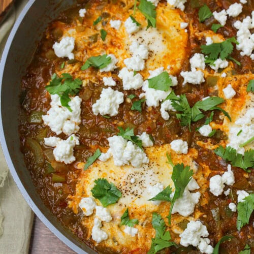 Green shakshuka with eggs, goat cheese, and cilantro in a ceramic skillet.