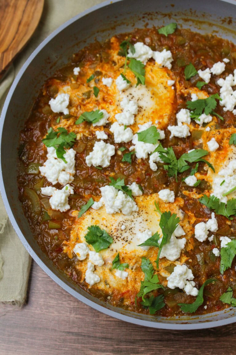 Green shakshuka with eggs, goat cheese, and cilantro in a ceramic skillet.