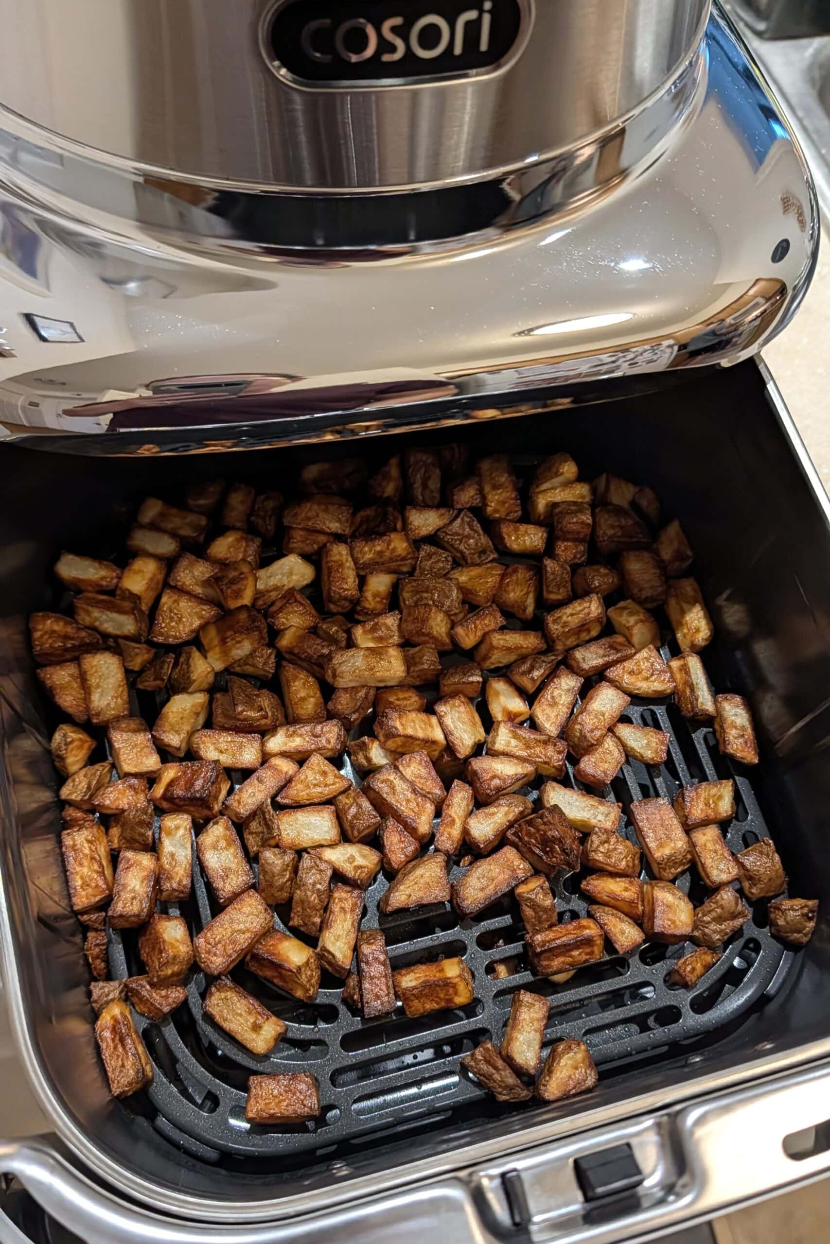 Crispy cubed potatoes in a stainless steel air fryer.
