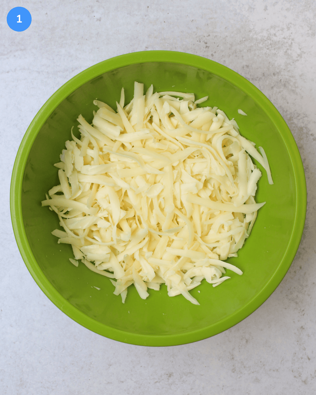 A green mixing bowl of shredded cheese.