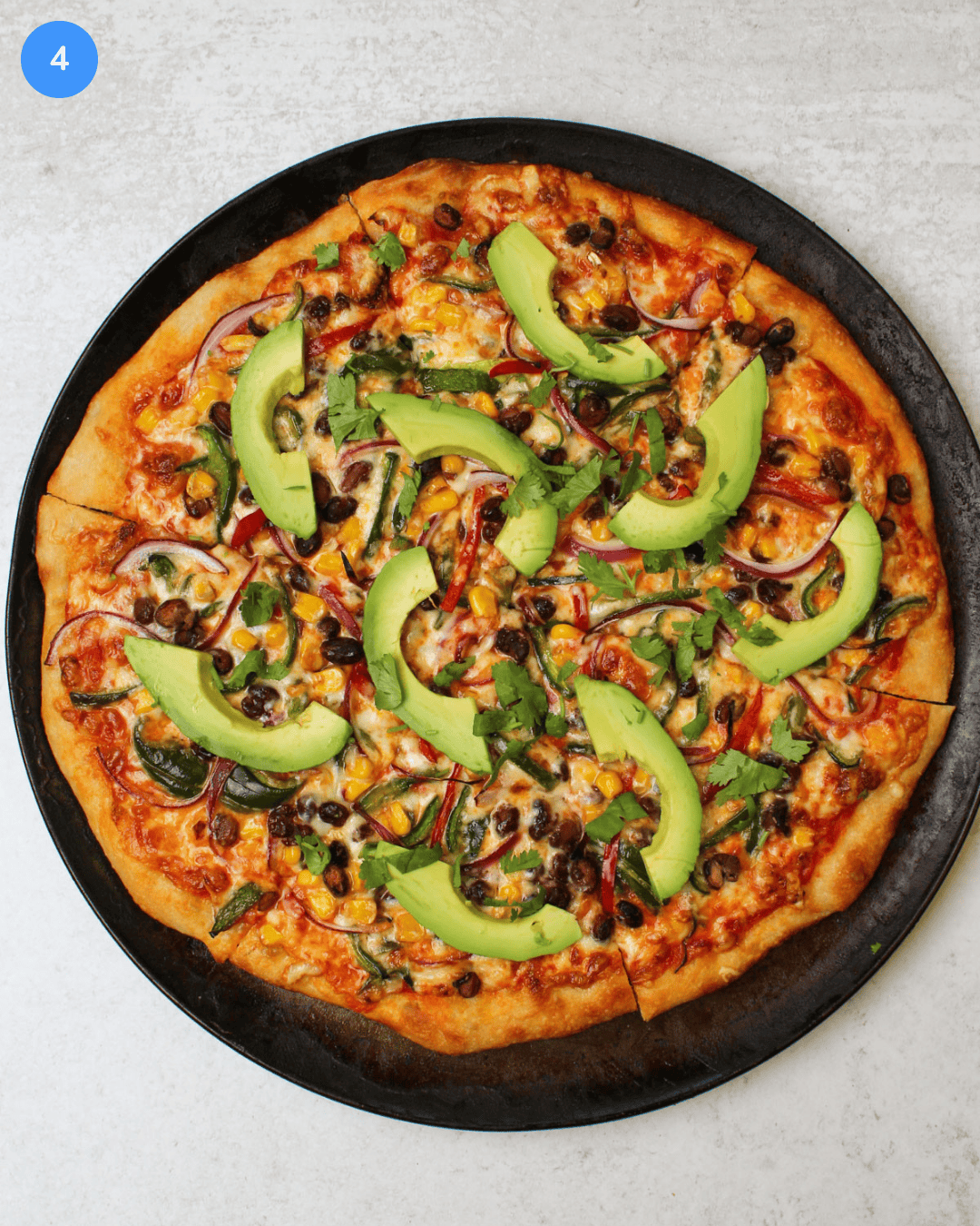 A freshly baked southwest veggie pizza topped with fresh avocado slices and cilantro.