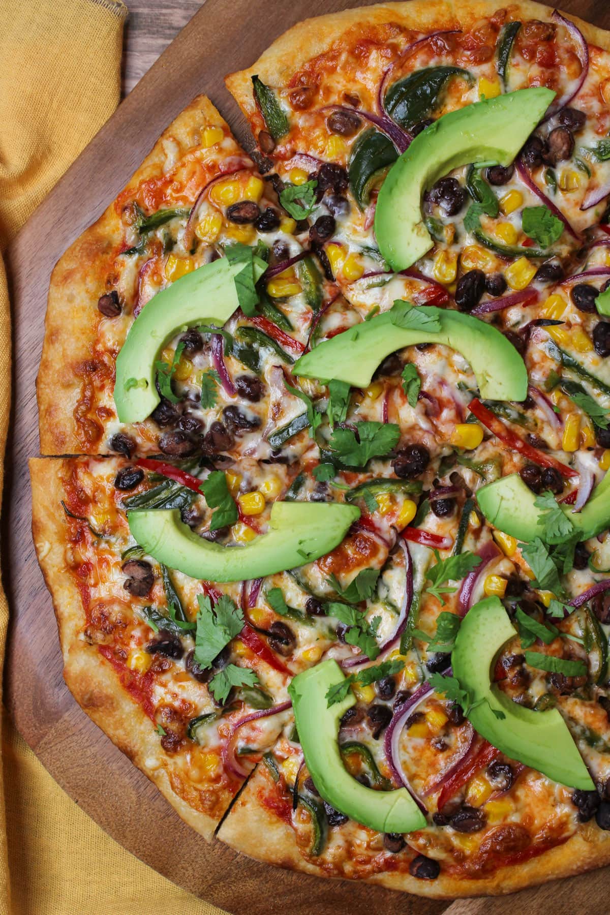 A southwest veggie pizza with golden brown crust and fresh avocado slices served on a wooden pizza peel.