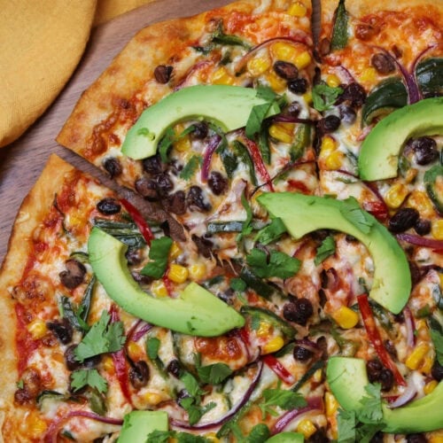 A freshly baked veggie pizza with black beans, corn, peppers, onion, avocado slices, and cilantro.