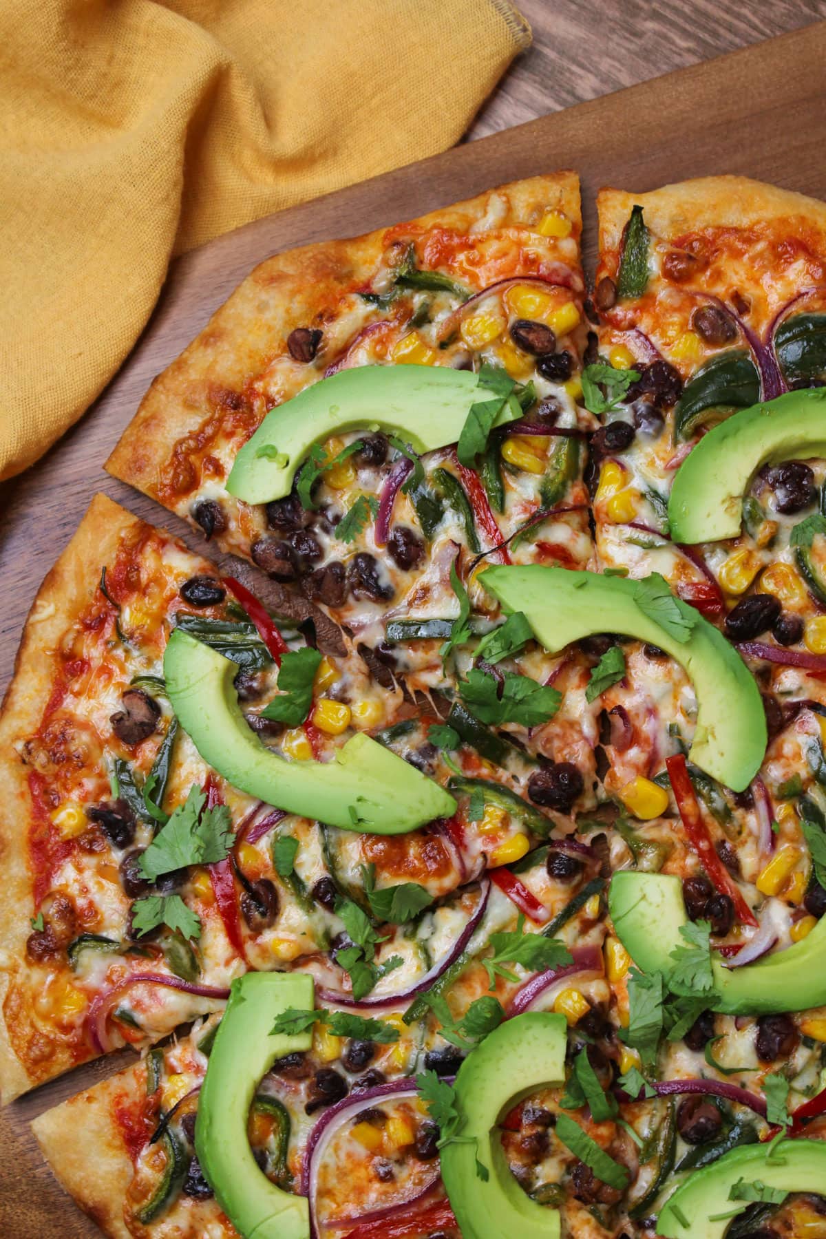 A freshly baked veggie pizza with black beans, corn, peppers, onion, avocado slices, and cilantro.