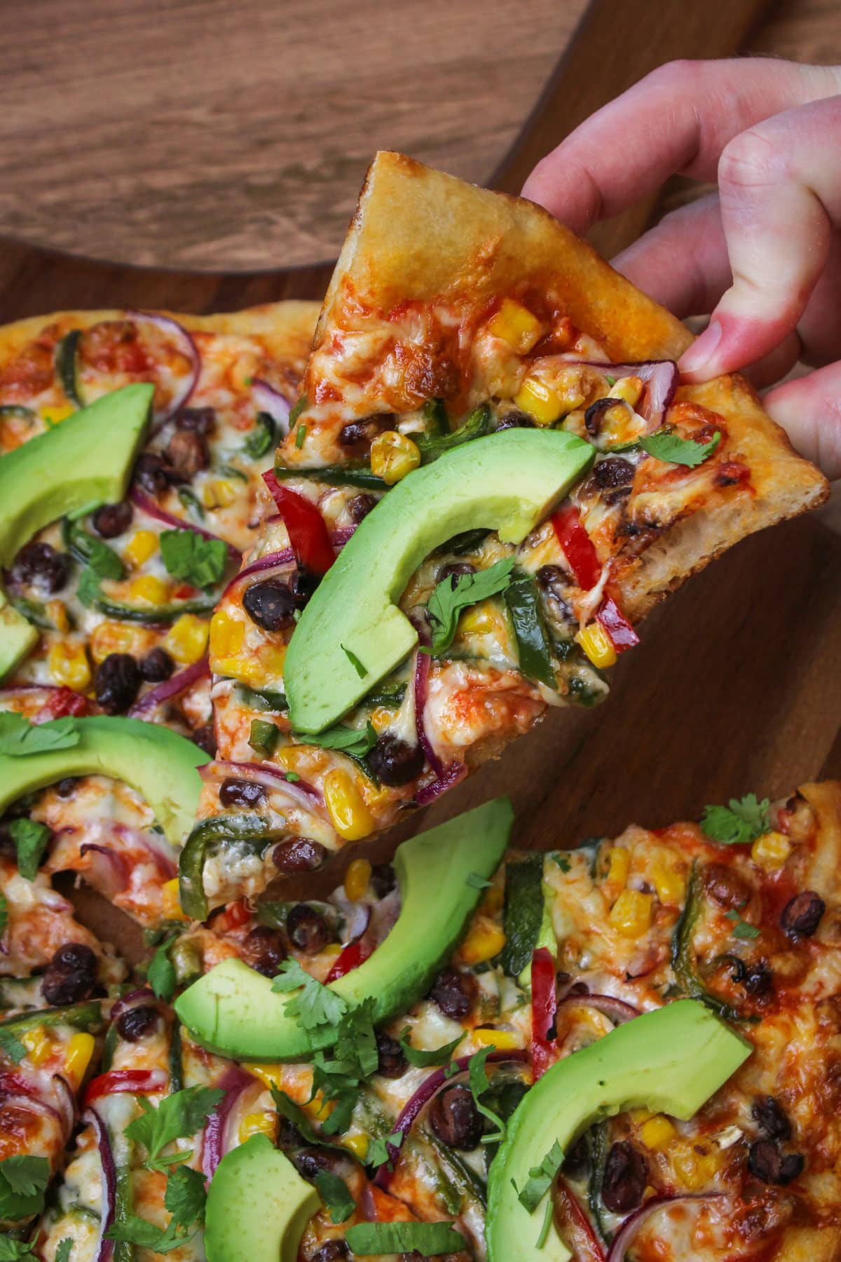 A slice of southwest veggie pizza topped with avocado and cilantro.