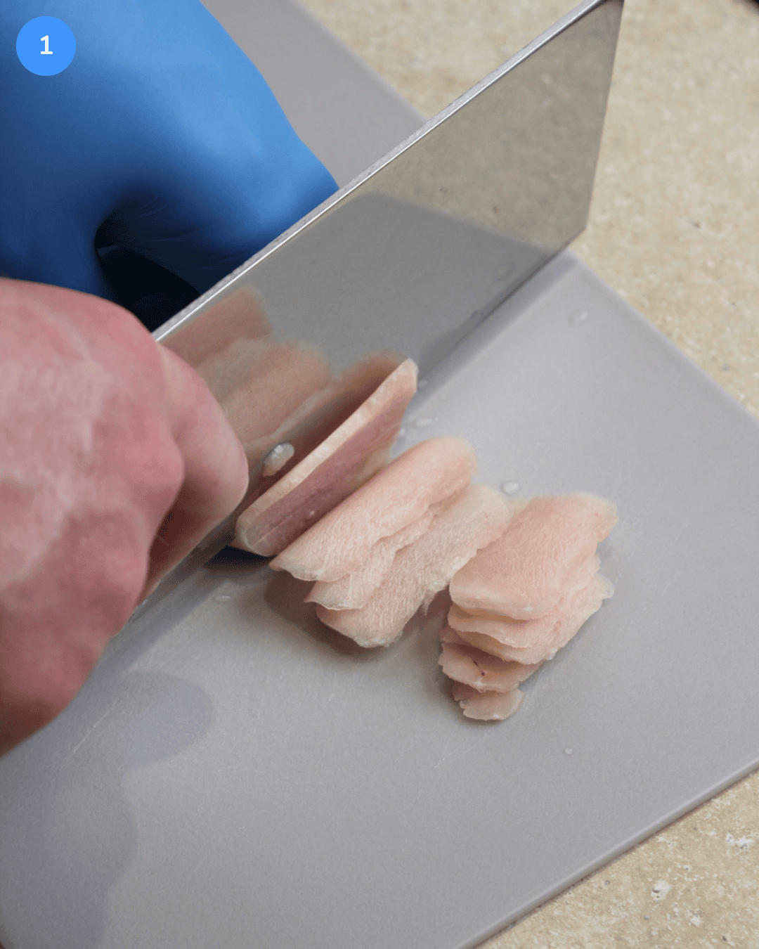 Slicing partially thawed chicken breast into thin shavings with a large Chinese chef's knife.