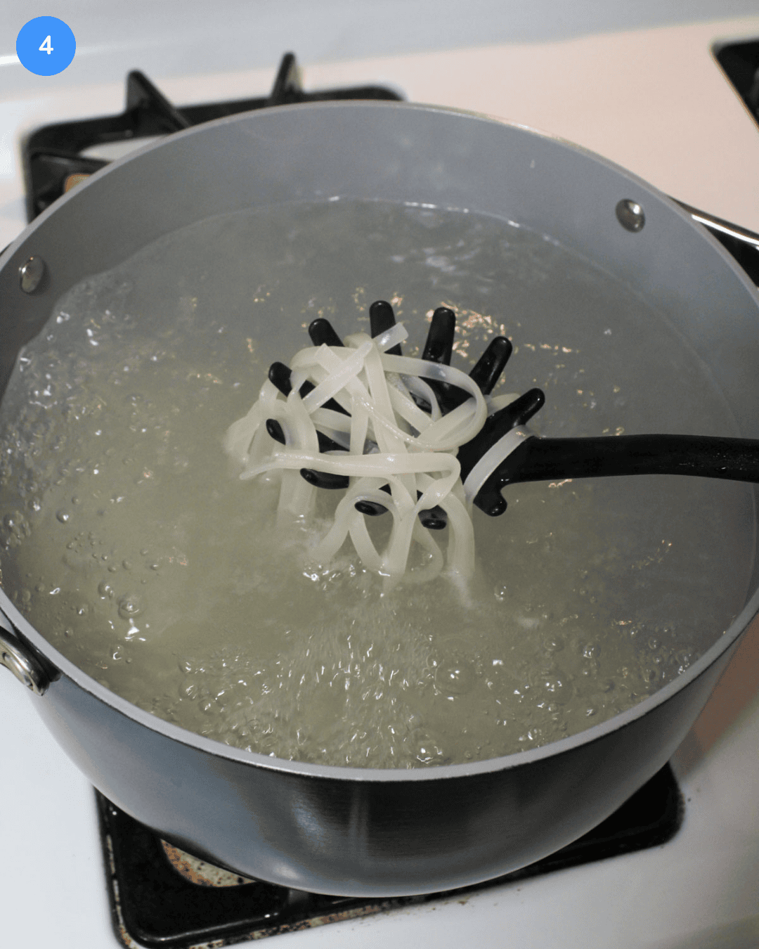 A large pot of Thai rice noodles boiling on the stove.