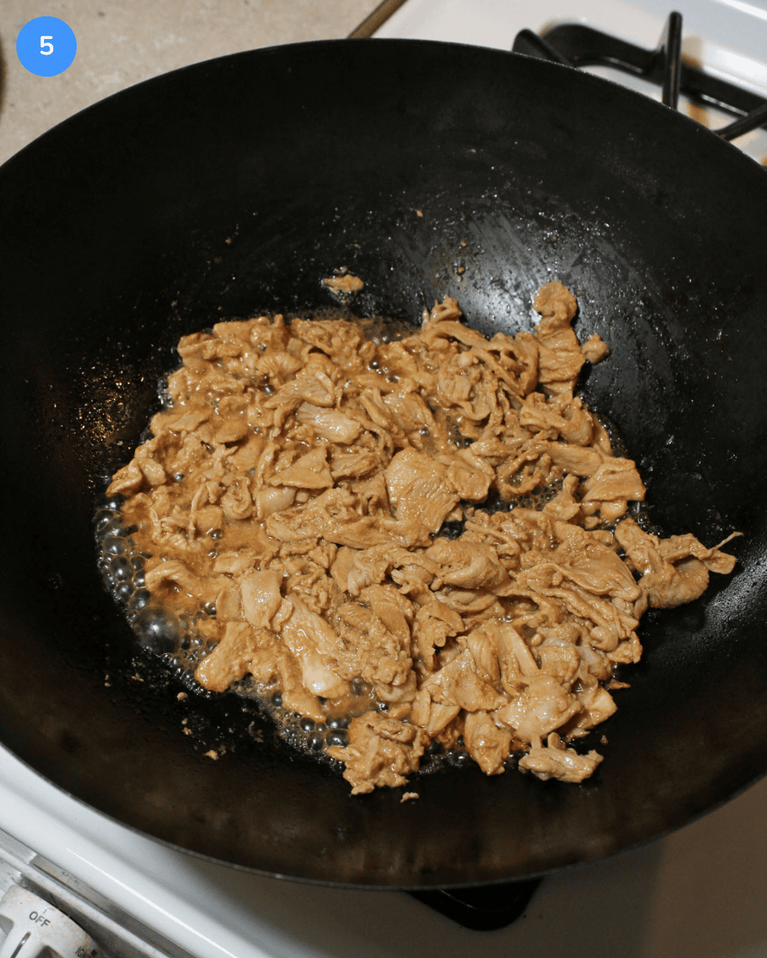 A carbon steel wok with thinly shaved marinated chicken cooking in it.