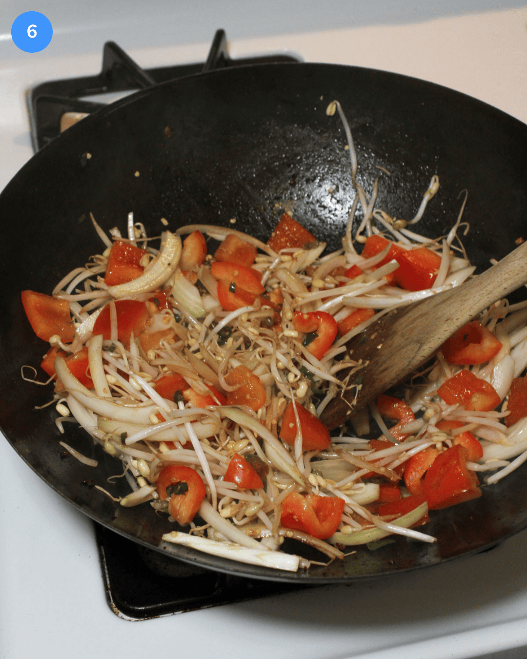 A carbon steel wok with fresh peppers, mung bean sprouts, and onion cooking in it on the stove.