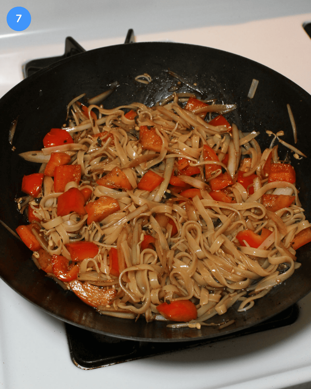 A carbon steel wok of Thai drunken noodles with veggies cooking on the stove.