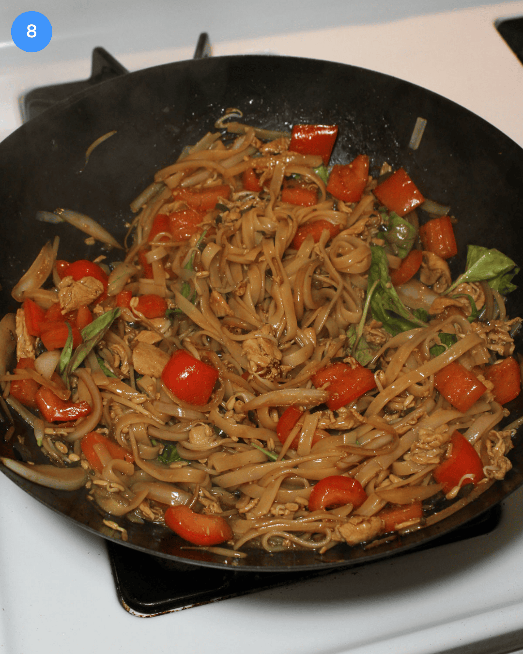 A wok full of Thai drunken noodles and veggies with thinly sliced chicken stirred in.