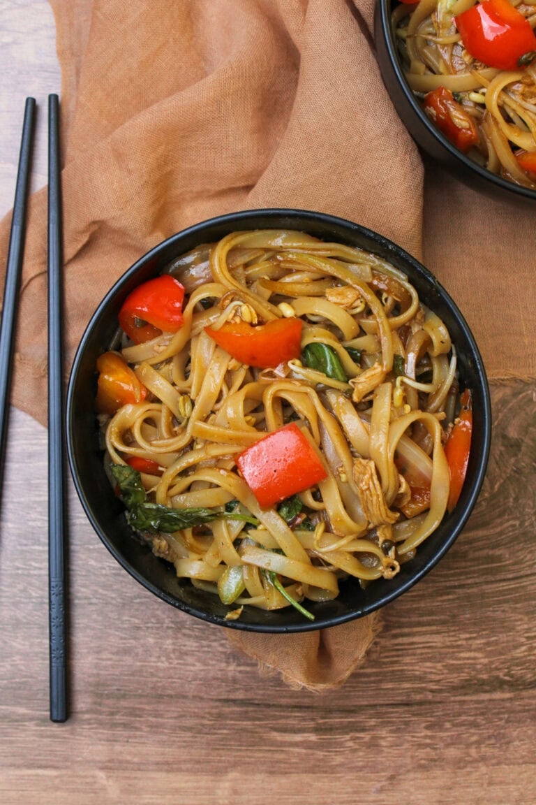 A black bowl of Thai chicken drunken noodles with chopsticks next to it.