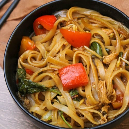 A black stone bowl of Thai drunken noodles with bell pepper, thai chilies, chicken, and fresh basil.