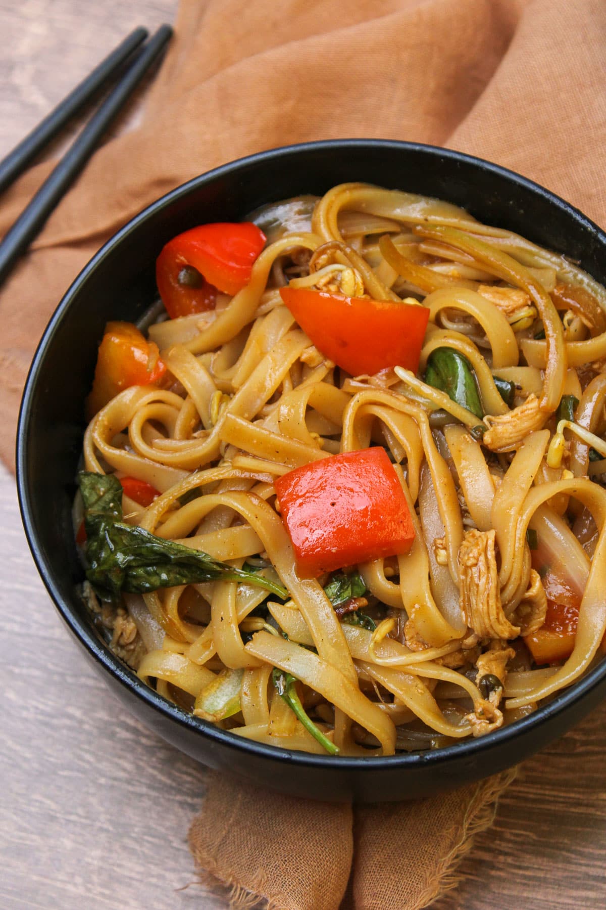 A black stone bowl of Thai drunken noodles with bell pepper, thai chilies, chicken, and fresh basil.