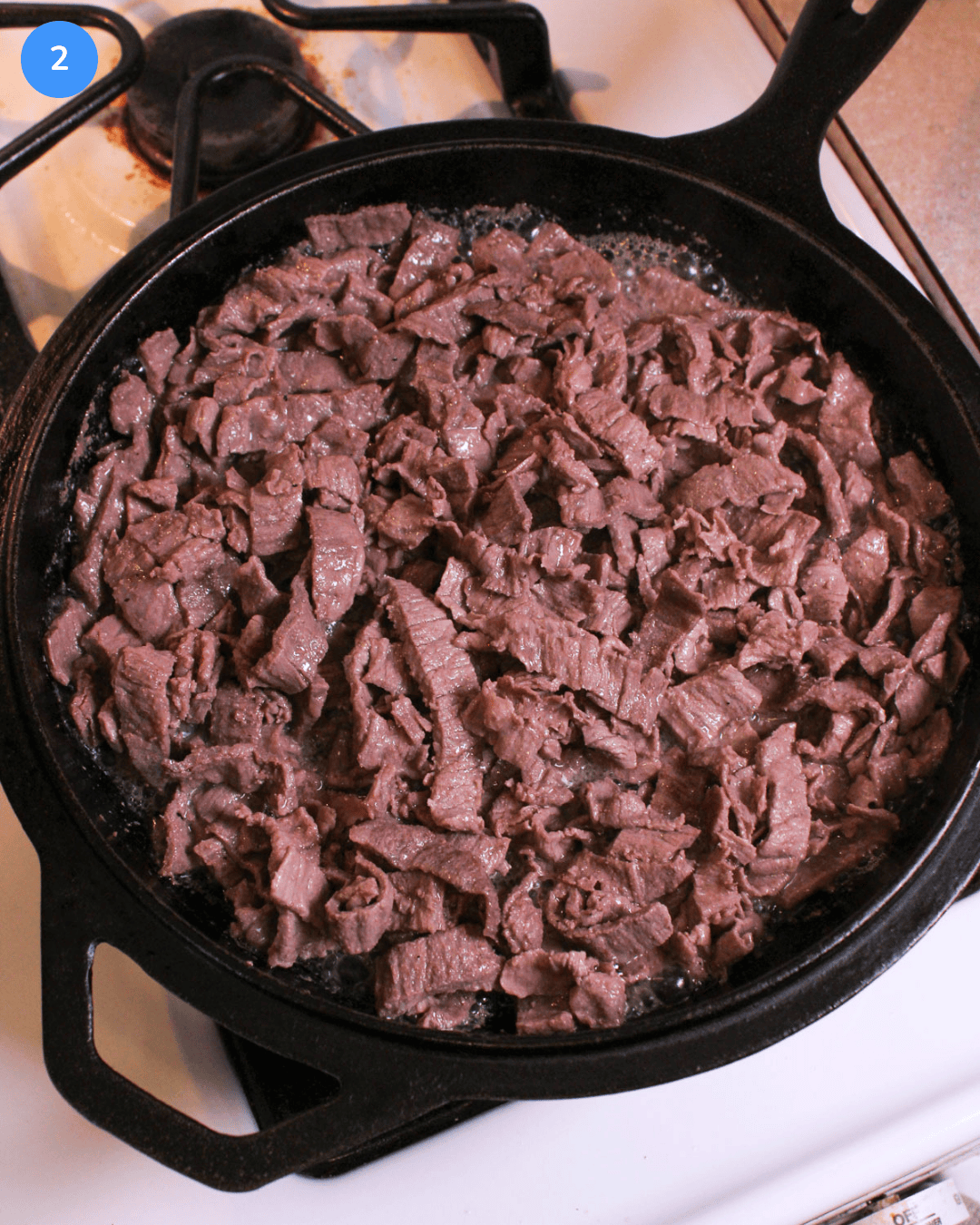 Thinly shaved steak cooking in a cast iron skillet on the stove.