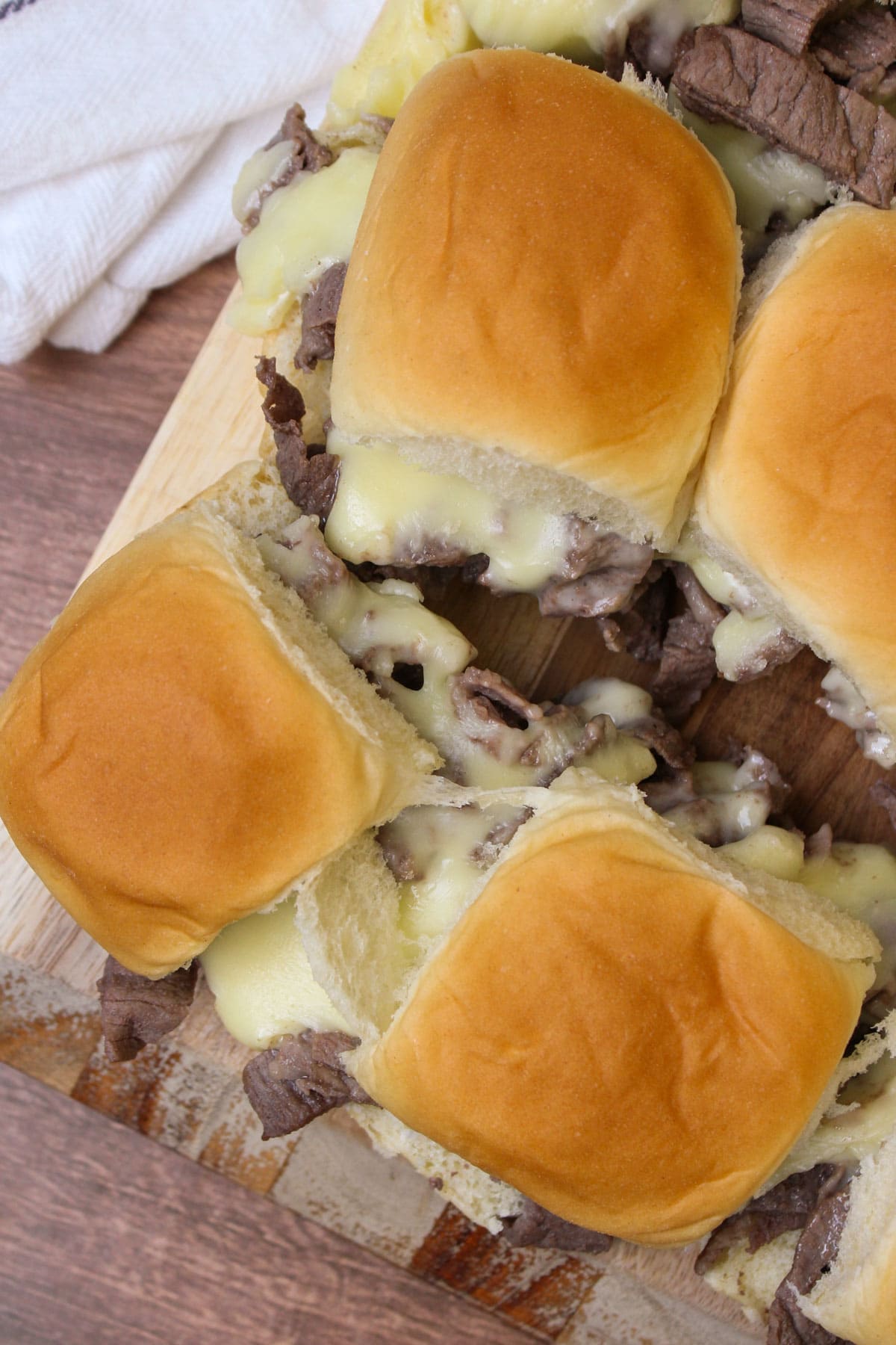A wood serving board of philly cheesesteak sliders oozing with american cheese sauce.