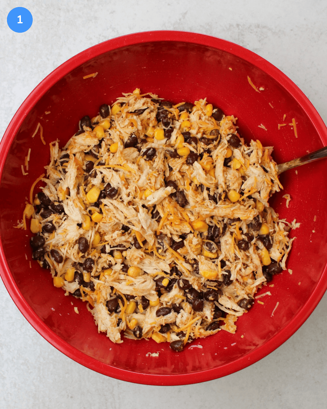 A large mixing bowl filled with shredded chicken, black beans, corn, and mexican cheese.
