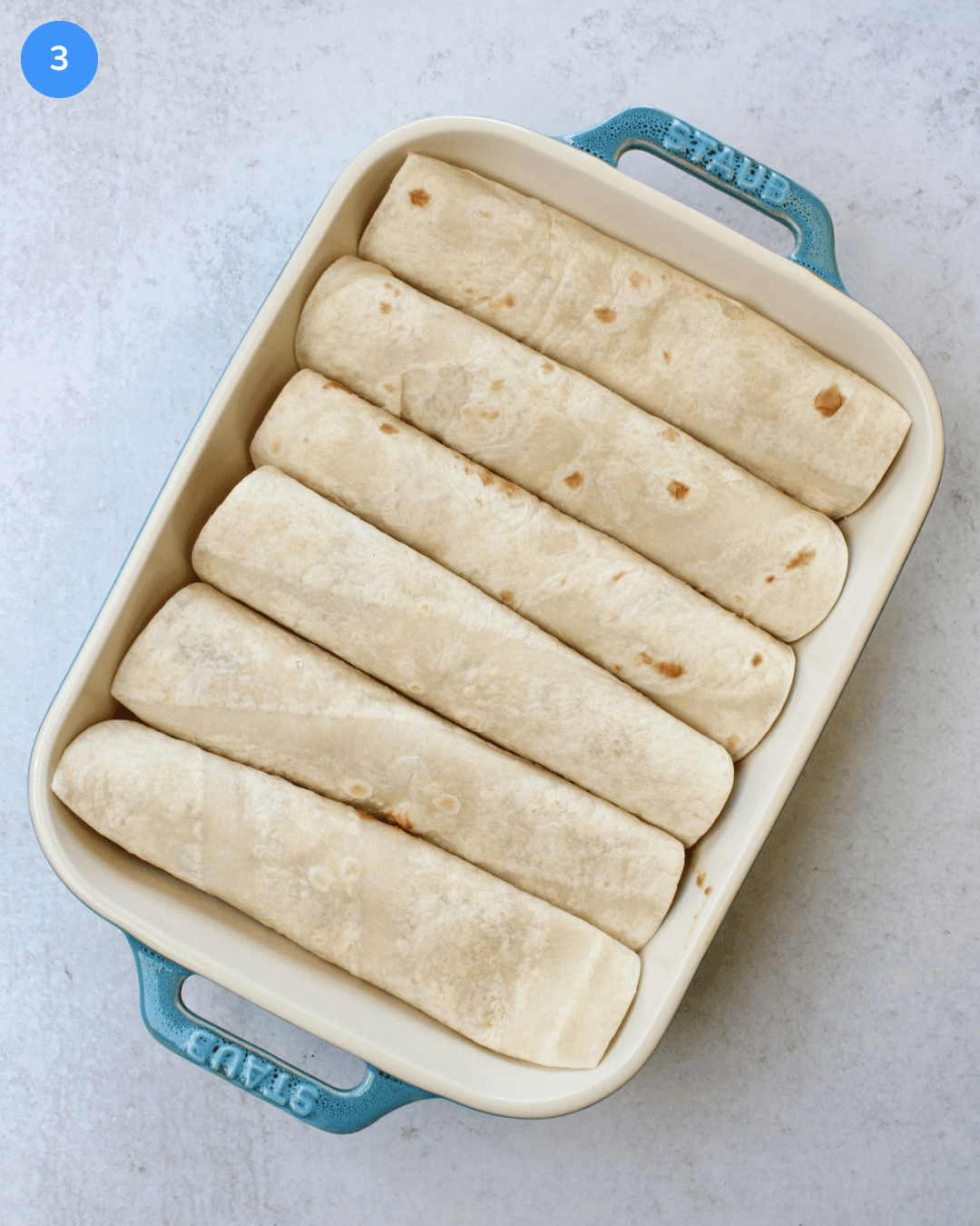 A ceramic baking dish filled with 6 rolled enchiladas in flour tortillas.