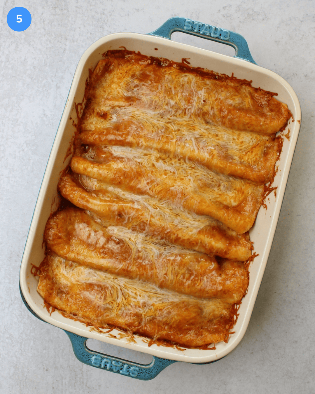A freshly baked dish of saucy red chicken enchiladas topped with gooey cheese.