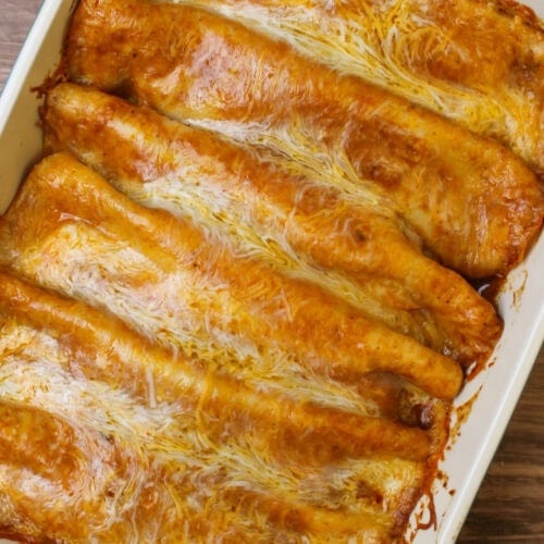A ceramic baking dish of freshly cooked saucy red chicken enchiladas.