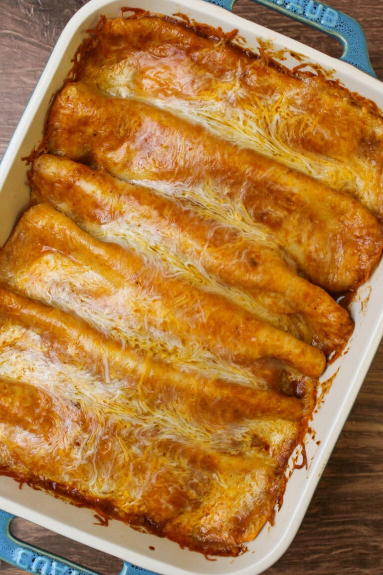 A ceramic baking dish of freshly cooked saucy red chicken enchiladas.