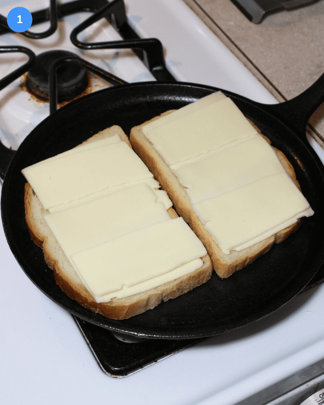 Two slices of sourdough with american cheese on a cast iron griddle on the stove.