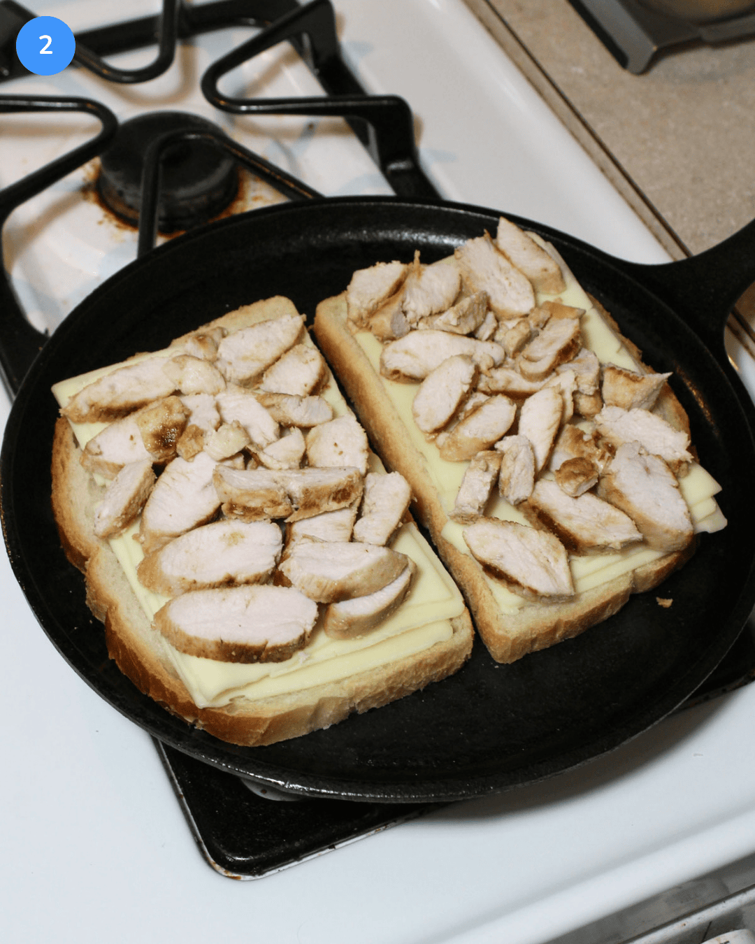 Two slices of sourdough topped with american cheese and grilled chicken on a griddle.