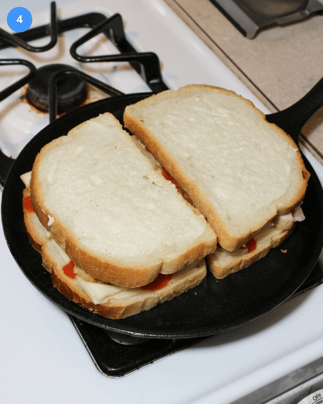 Two buffalo chicken grilled cheese sandwiches cooking on a cast iron griddle.