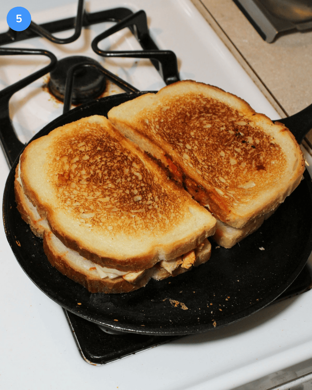 Two crispy sourdough buffalo chicken grilled cheese sandwiches on a cast iron griddle.
