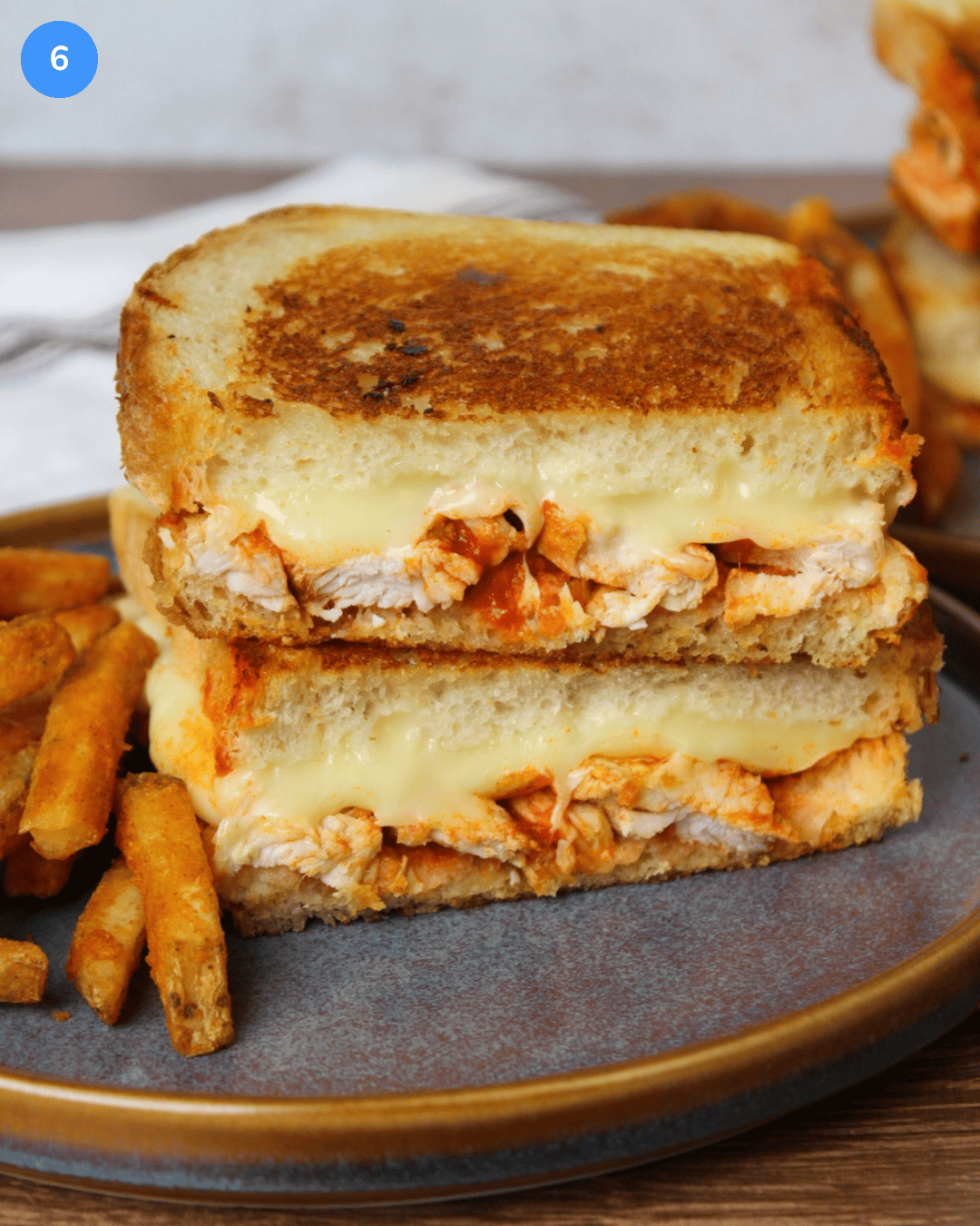 A crispy, golden brown buffalo chicken grilled cheese sliced in half and stacked on a blue stone plate.