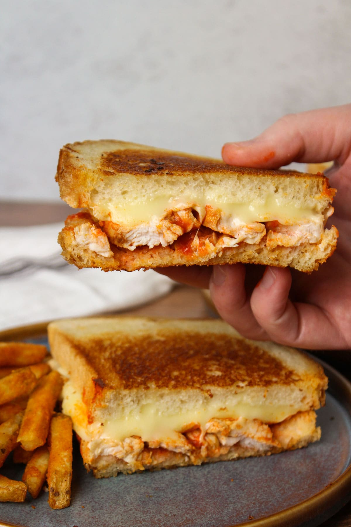 Half of a saucy buffalo chicken grilled cheese being picked up from a blue stone plate.